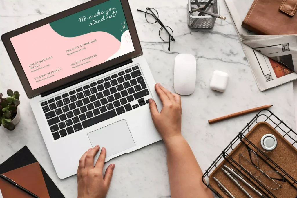 A woman's hands typing on a laptop, set against a vibrant pink and green background, symbolizing digital marketing